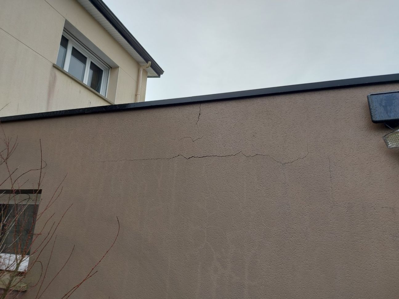 Fissures infiltrantes et décollement de l'enduit sur le chaînage et l'acrotère béton par manque d'accrochage par gobetis